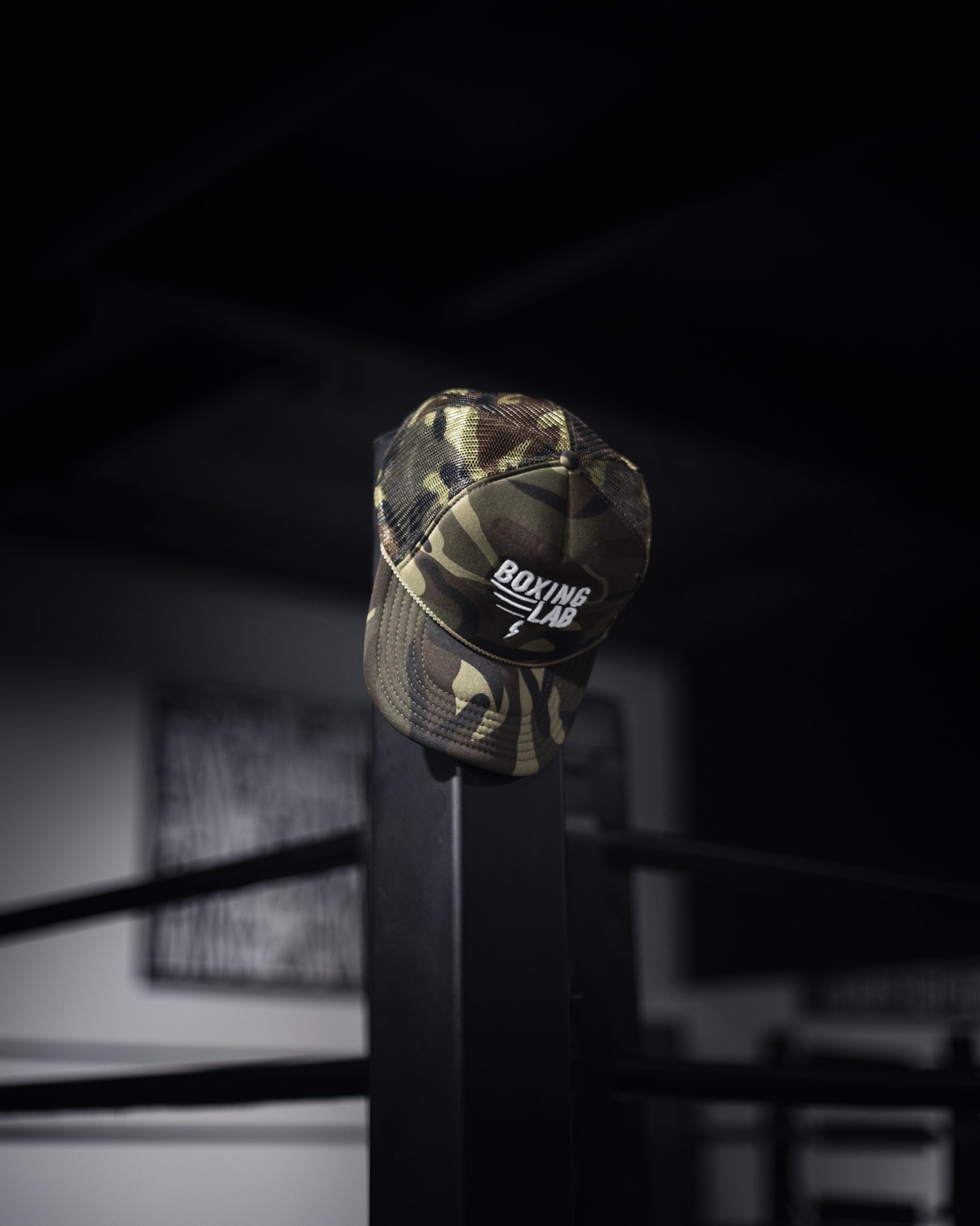 Boxing Lab camouflage trucker hat on a gym rack