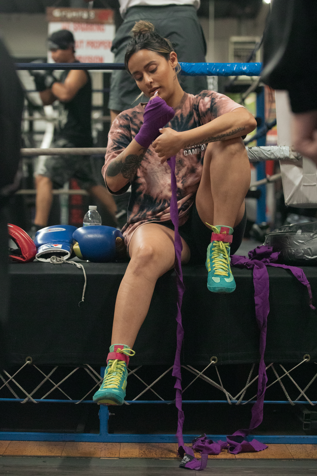 Fighter wrapping her hands with purple wraps at the edge of a boxing ring